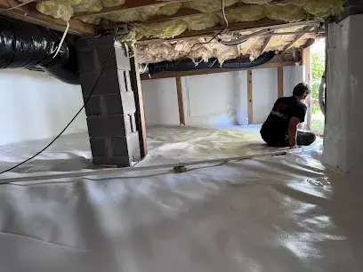 Worker kneeling on a new white vapor barrier beneath exposed joists and insulation