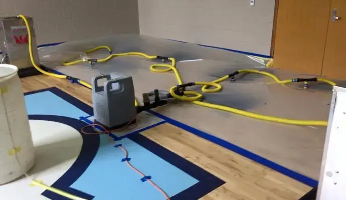 Drying panels with yellow hoses taped down across a gym basketball floor