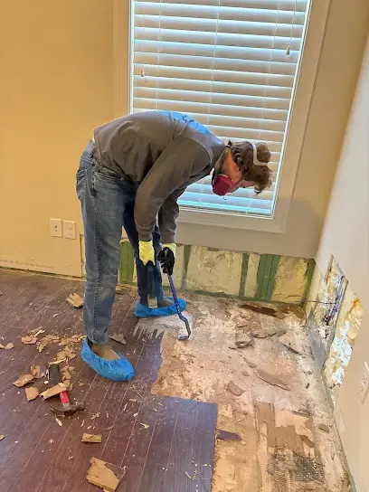 Masked worker lifting wood flooring boards beside a wall that has been opened