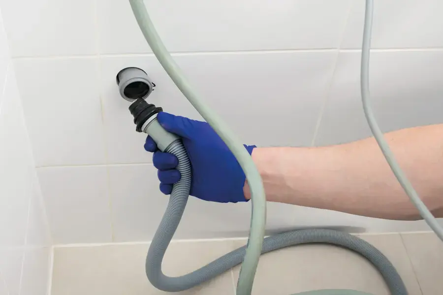 Gloved hand holding a leaking washing machine drain hose