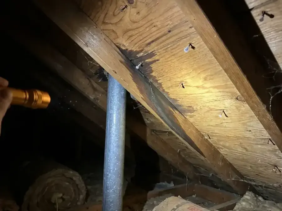 Water-stained roof rafter in a Huntersville attic under a flashlight