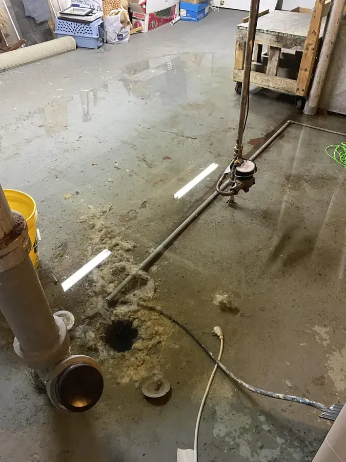 Sewage backup water spread around an open floor drain on a basement slab